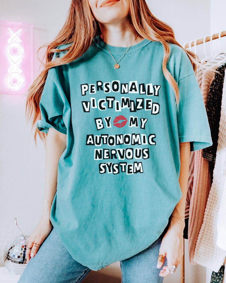 May include: A teal blue t-shirt with the text "PERSONALLY VICTIMIZED BY 💋 MY AUTONOMIC NERVOUS SYSTEM" printed in black.