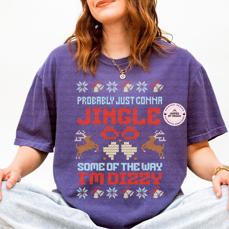Peut inclure: T-shirt violet avec un motif festif. Le t-shirt affiche le texte "Probably Just Comma Jingle All The Way I'm Dizzy" en rouge et bleu, avec des motifs de rennes et de flocons de neige. Le t-shirt a une coupe ample.