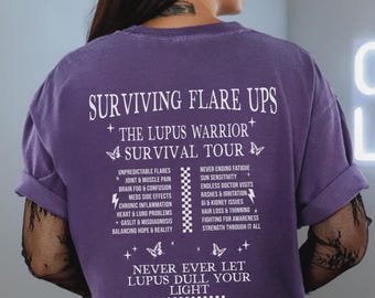Op de afbeelding: Paars T-shirt met witte tekst die "Surviving Flare Ups + The Lupus Warrior + Survival Tour" luidt en symptomen van lupus opsomt. De onderkant van het shirt luidt "Never Ever Let Lupus Dull Your Light".