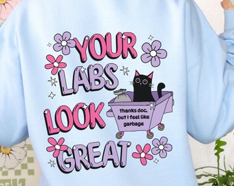 May include: Light blue sweatshirt with a graphic print of a black cat sitting in a purple garbage can with the text "YOUR LABS LOOK GREAT" and "thanks doc, but I feel like garbage".