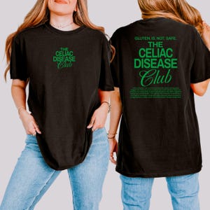 Op de afbeelding: Zwart t-shirt met de tekst "THE CELIAC DISEASE Club" in groen op de voor- en achterkant. De achterkant van het shirt heeft ook de tekst "GLUTEN, IS. NOT. SAFE." en een alinea tekst in het groen.