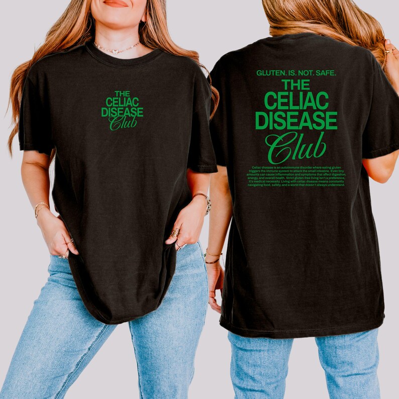 Op de afbeelding: Zwart t-shirt met de tekst "THE CELIAC DISEASE Club" in groen op de voor- en achterkant. De achterkant van het shirt heeft ook de tekst "GLUTEN, IS. NOT. SAFE." en een alinea tekst in het groen.