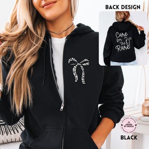 May include: Black zip-up hoodie with a white and zebra-striped bow design on the front. The back of the hoodie features the text "Care for the Rare" in white script. The hoodie is a casual garment.