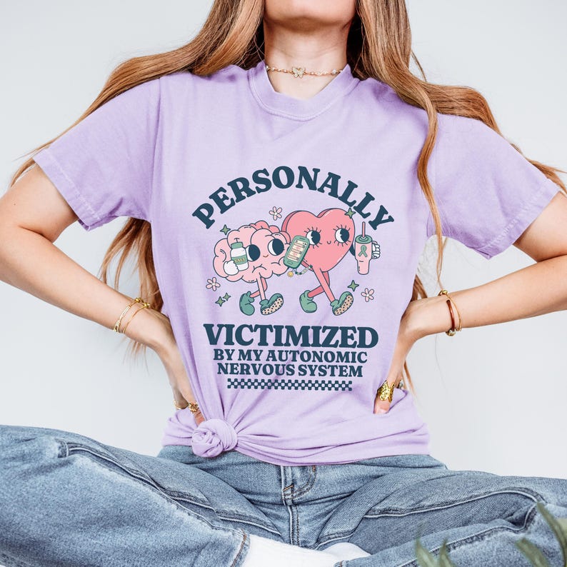 K&ouml;nnte beinhalten: Ein lila T-Shirt mit einem Motiv aus einem Gehirn und einem Herzen, die Getr&auml;nke halten. Der Text auf dem Shirt lautet "PERSONALLY VICTIMIZED BY MY AUTONOMIC NERVOUS SYSTEM".