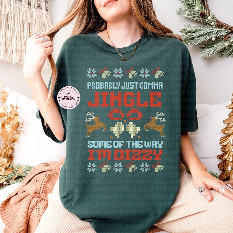 Peut inclure: T-shirt vert fonc&eacute; avec un motif festif. Le t-shirt pr&eacute;sente le texte "Probably Just Comma Jingle All The Way I'm Dizzy" en rouge et blanc, ainsi que des flocons de neige, des cloches, des rennes et des tr&egrave;fles. Un autocollant rond est visible.