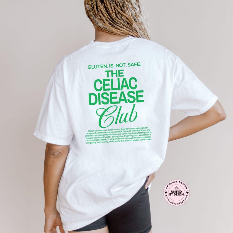Op de afbeelding: Wit T-shirt met groene tekst: "GLUTEN. IS. NOT. SAFE. THE CELIAC DISEASE Club." Het shirt bevat ook een beschrijving van coeliakie. Onderdeel van de collectie "UNIFIED BY DESIGN AUTHENTIC CREATIONS".