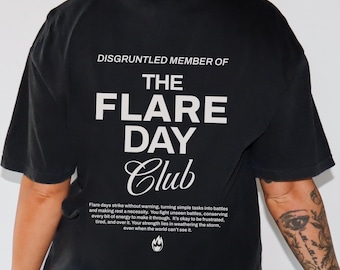 Puede incluir: Camiseta negra con texto blanco que dice "Disgruntled Member of The Flare Day Club". El texto está centrado en la parte posterior de la camiseta. Debajo del texto hay una descripción más pequeña en blanco sobre "Flare Days" y un pequeño gráfico de llama blanca.