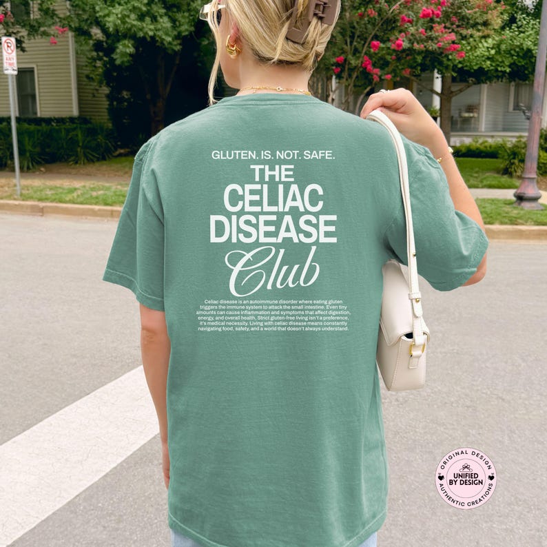 Op de afbeelding: Een groen t-shirt met witte tekst met de tekst "GLUTEN. IS. NOT. SAFE. THE CELIAC DISEASE Club". Het shirt heeft ook een beschrijving van Coeliakie. Het shirt is een casual stijl met korte mouwen.