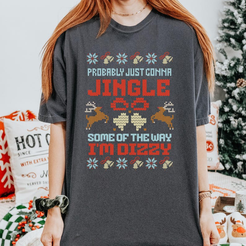 Peut inclure: T-shirt gris fonc&eacute; avec un motif de No&euml;l. Le texte se lit &laquo;&nbsp;Probably Just Comma Jingle Some of the Way I'm Dizzy&nbsp;&raquo; en rouge et bleu, avec des graphiques de rennes et de flocons de neige. Un article de v&ecirc;tement festif.