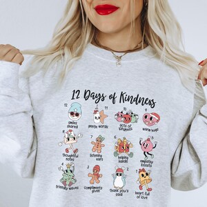May include: A gray sweatshirt with a graphic design of 12 days of kindness. Each day is represented by a number and a cartoon illustration with a corresponding act of kindness. The text "12 Days of Kindness" is at the top of the design.