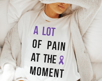 May include: White t-shirt with the text "A lot of pain at the moment" and a purple ribbon.