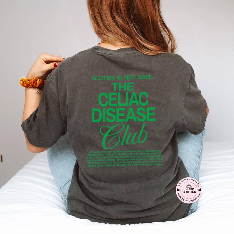 Op de afbeelding: Donkergrijs T-shirt met de groene tekst "GLUTEN IS NOT SAFE. THE CELIAC DISEASE CLUB". Het shirt heeft ook een beschrijving van Coeliakie in het groen. Het shirt heeft een comfortabele pasvorm.