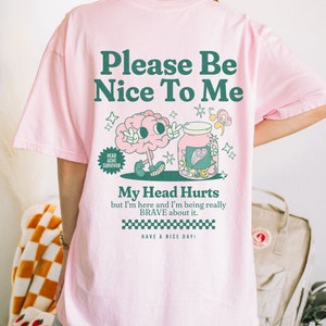 May include: Pink t-shirt with a green cartoon brain and a jar with hearts and stars. The text on the shirt reads "Please Be Nice To Me", "Head Ache Survivor", "My Head Hurts but I'm here and I'm being really BRAVE about it. HAVE A NICE DAY!"