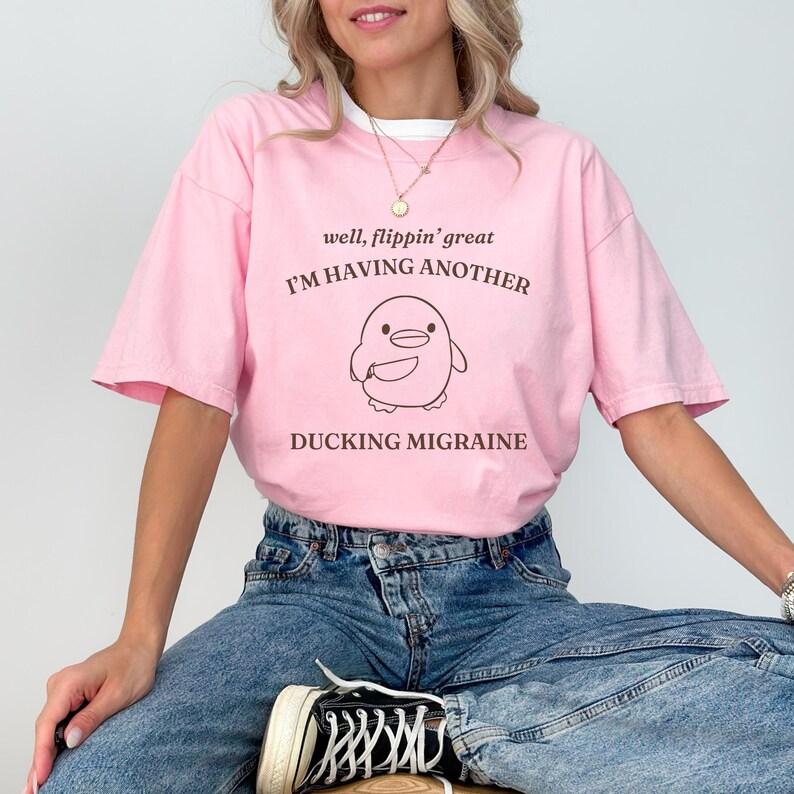 May include: Pink t-shirt with a cartoon duck holding a knife and the text "well, flippin' great I'M HAVING ANOTHER DUCKING MIGRAINE"