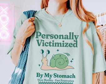 Puede incluir: Una camiseta azul claro con un gráfico de caracol verde y el texto "Personalmente victimizado por mi estómago Motilidad lenta - Frustración rápida Club de concienciación sobre la gastroparesia".