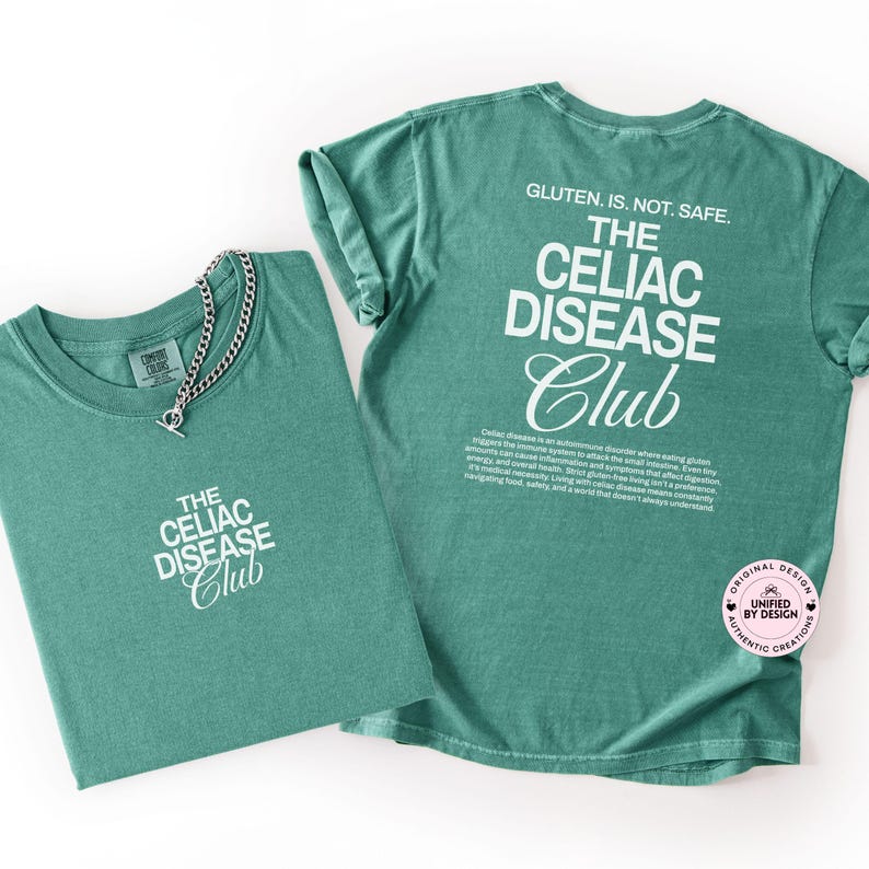 Op de afbeelding: Twee groene t-shirts met witte tekst "THE CELIAC DISEASE Club". E&eacute;n shirt heeft een zilveren ketting. De achterkant van &eacute;&eacute;n shirt leest "GLUTEN. IS. NOT. SAFE." en heeft een beschrijving van Coeliakie.