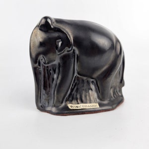 May include: A black ceramic sculpture of a bear sitting on its haunches. The bear is made in a stylised, abstract style. The sculpture is signed "Otto Keramik" on the bottom.