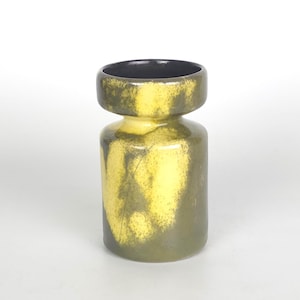 Könnte beinhalten: Eine zylindrische Keramikvase mit einem breiten, ausgestellten Rand und einem schmalen Hals. Die Außenfläche zeigt ein gesprenkeltes Glasurmuster mit vermischten Farbtönen in Olivgrün und hellem Gelb, während das Innere des Randes schwarz ist.