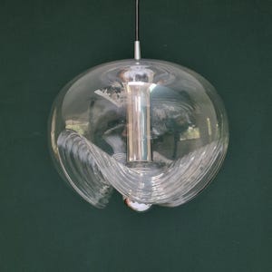 May include: Clear glass pendant light with a spherical shape and a swirling, textured design. The light fixture has a silver-colored metal base and a black cord for hanging. The overall design is modern and decorative.