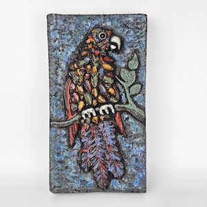 Può includere: Una piastrella da parete in ceramica colorata che raffigura un pappagallo appollaiato su un ramo. Il pappagallo è rosso, giallo, verde e blu con un occhio bianco. Lo sfondo è blu e nero screziato.