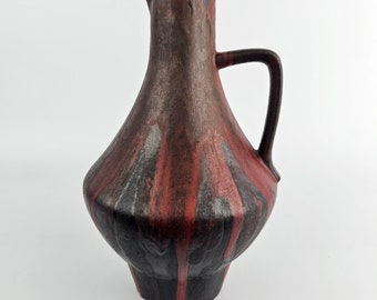 May include: A brown ceramic pitcher with a red and silver glaze. The pitcher has a wide base and a narrow neck with a handle.