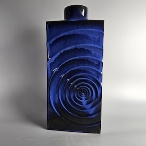 Könnte beinhalten: Eine hohe, rechteckige blaue Keramikvase mit einem wirbelnden, konzentrischen Kreis-Muster.