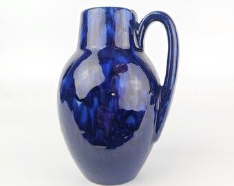 May include: A blue ceramic pitcher with a mottled glaze. The pitcher has a round body and a handle.