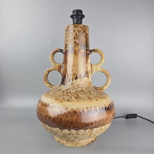 Peut inclure: Lampe de table en céramique avec glaçure mouchetée marron et beige. La lampe a une douille en haut et deux ensembles de poignées en boucle. La lampe mesure environ 46 cm de haut.