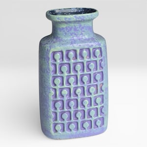 Puede incluir: Un jarrón rectangular de cerámica con una superficie texturizada y un patrón repetido de formas estilizadas. El jarrón es principalmente lavanda y verde claro, con un interior y borde azul oscuro. El diseño es de estilo retro, moderno de mediados de siglo.
