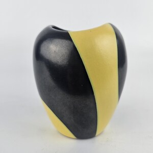 May include: A small, black and yellow ceramic vase with a curved shape. The vase has a striped pattern.