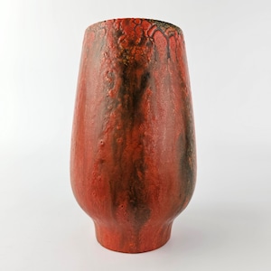 Puede incluir: Un jarrón de cerámica texturizada en tonos rojos, negros y marrones. El jarrón tiene una base ancha que se estrecha hacia arriba, con un borde acampanado. La superficie tiene una textura rugosa, similar a la lava, que le da un aspecto artesanal. Aproximadamente 25 cm de altura.