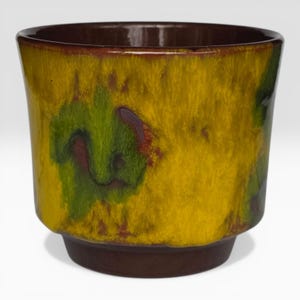May include: A ceramic planter with a brown base and rim, and a yellow body with green and red accents. The planter has a slightly flared shape and a smooth, glossy finish. The design is abstract and organic, with a textured appearance.