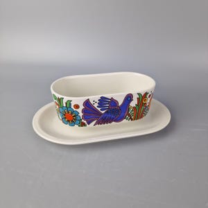 Puede incluir: Salsera de cerámica blanca con un diseño floral y un pájaro coloridos. La salsera tiene un plato a juego.