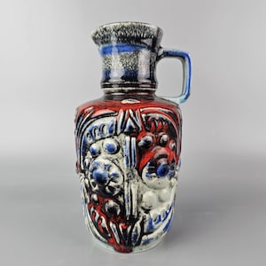 Può includere: Un vaso in ceramica rosso, blu e bianco con un design testurizzato. Il vaso ha un manico e una bocca larga.