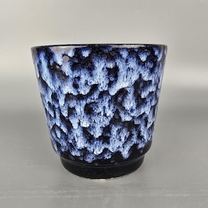 Peut inclure: Un pot de plante en céramique avec un glaçage réactif texturé dans les tons bleu marine et blanc. Le pot a une base sombre et un bord légèrement évasé. L'extérieur présente un motif organique unique, ajoutant un intérêt visuel au design.