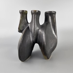 Puede incluir: Un jarrón de cerámica negro y verde con tres aberturas. El jarrón tiene una forma abstracta y orgánica.