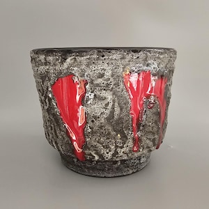 May include: A ceramic planter with a textured, gray surface and red glaze accents. The planter has a wide, round opening and a slightly flared lip.