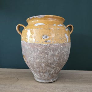 May include: An aged ceramic vase with two handles. The top section is a faded yellow, and the bottom is a weathered brown. The vase has a distressed look, with signs of wear and age, enhancing its vintage appeal. A decorative piece for the home.