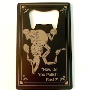 May include: Black bottle opener with a silver robot illustration and the text "How Do You Polish Rust?" The opener has a decorative border and a built-in bottle cap remover.
