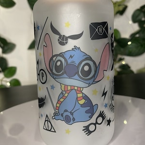 Puede incluir: Vaso de vidrio esmerilado con tapa de bambú, con un personaje de dibujos animados azul con gafas y bufanda, rodeado de gráficos temáticos de Harry Potter. El vaso tiene una capacidad de aproximadamente 470 ml.