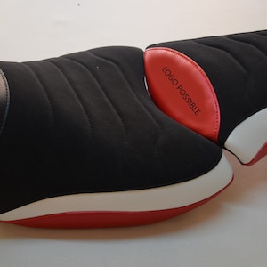 Può includere: Sella da moto nera con base rossa e bianca. La sella presenta un motivo trapuntato e una sezione nera strutturata. Il testo "LOGO POSSIBLE" è stampato su una sezione rossa della sella.