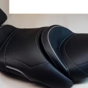 Può includere: Sella da moto nera con schienale per passeggero. Il sedile ha un design sagomato con cuciture bianche. Il sedile è realizzato in un materiale liscio e resistente.