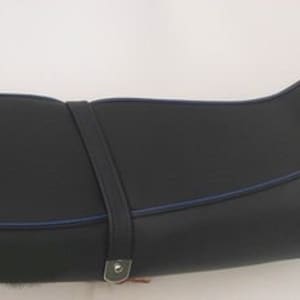Op de afbeelding: Een zwarte motorzadel met een blauwe sierstreep en een bevestigingsriem. De zitting heeft een gebogen ontwerp en is gemaakt van een glad, duurzaam materiaal. De riem is vastgezet met een metalen gesp.