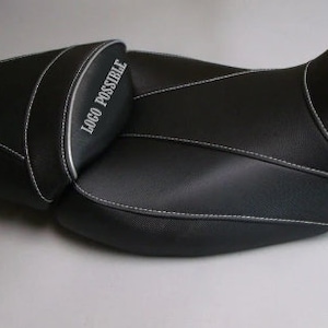 Può includere: Sella da moto nera con cuciture bianche e la scritta "LOGO POSSIBLE". La sella ha una superficie strutturata e un design curvo, con una sezione passeggero separata.