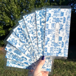 K&ouml;nnte beinhalten: Ein Satz von acht blauen und wei&szlig;en gemusterten Planer-Teilern mit durchsichtigen Plastikh&uuml;llen. Die Teiler zeigen ein sich wiederholendes Muster aus H&auml;usern und Blumen. Das Wort "airfare" ist auf einem der Teiler gedruckt.