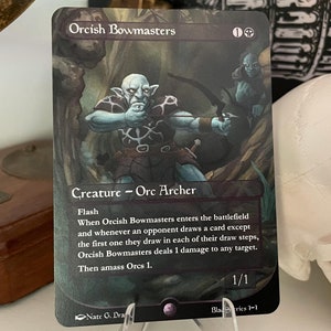 May include: A Magic: The Gathering card featuring an Orcish Bowmasters creature card with a blue and green illustration of an Orc archer. The card text reads "Flash. When Orcish Bowmasters enters the battlefield and whenever an opponent draws a card except the first one they draw in each of their draw steps, Orcish Bowmasters deals 1 damage to any target. Then amass Orcs 1."