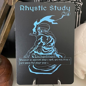 May include: A black card with blue text and a blue illustration of a person in a hooded robe. The card is titled "Rhystic Study" and has the text "Enchantment" and "Whenever an opponent plays a spell, you may draw a card unless that player pays 1."