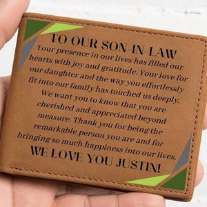 May include: A brown leather wallet with a green, yellow, and gray patterned design. The wallet has a message inside that reads "To our son-in-law. Your presence in our lives has filled our hearts with joy and gratitude. Your love for our daughter and the way you effortlessly fit into our family has touched us deeply. We want you to know that you are cherished and appreciated beyond measure. Thank you for being the remarkable person you are and for bringing so much happiness into our lives. We love you Justin!"
