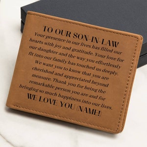 May include: A tan leather wallet with stitched edges. The wallet has the text "TO OUR SON-IN-LAW" and a heartfelt message engraved on the front. The message includes the words "WE LOVE YOU (NAME!)".