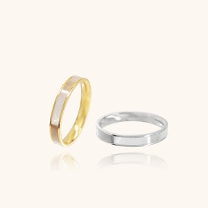 May include: Two rings, one gold and one silver, are displayed. The gold ring has a band of light pink and white, while the silver ring has a band of white. Both rings are simple and elegant, with a polished finish.